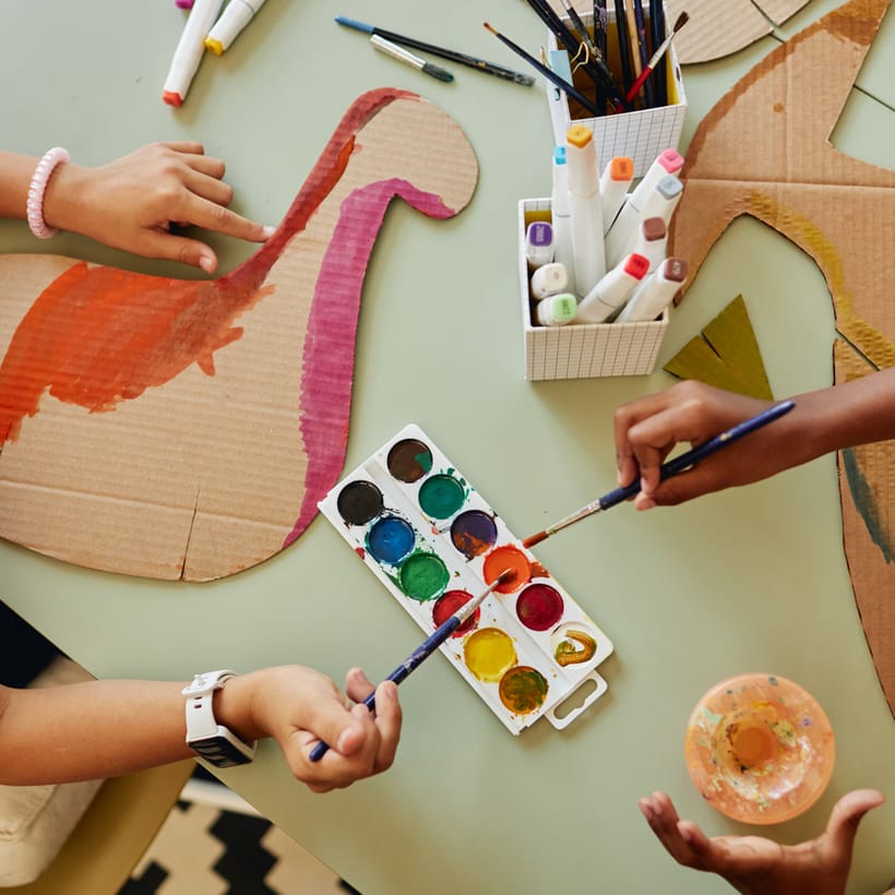 Children painting cardboard cut-outs with watercolours at a craft table